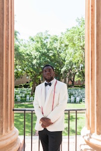 a man in a white tuxedo standing in front of columns